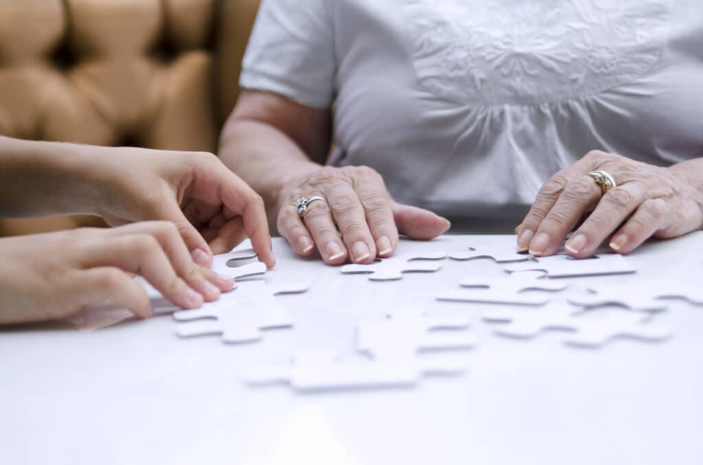 Old woman with one part of puzzle connecting with other shape on white table.Practicing brain in retirement